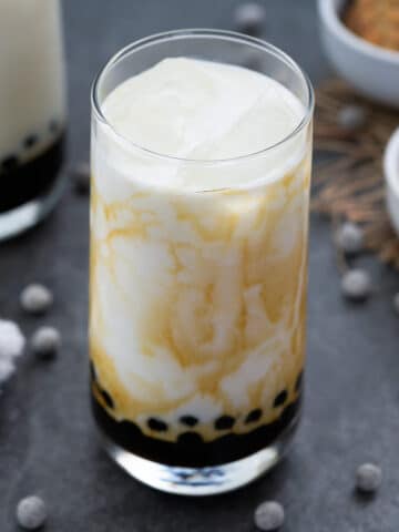 Brown Sugar boba milk served in a glass with boba pearls scattered around.