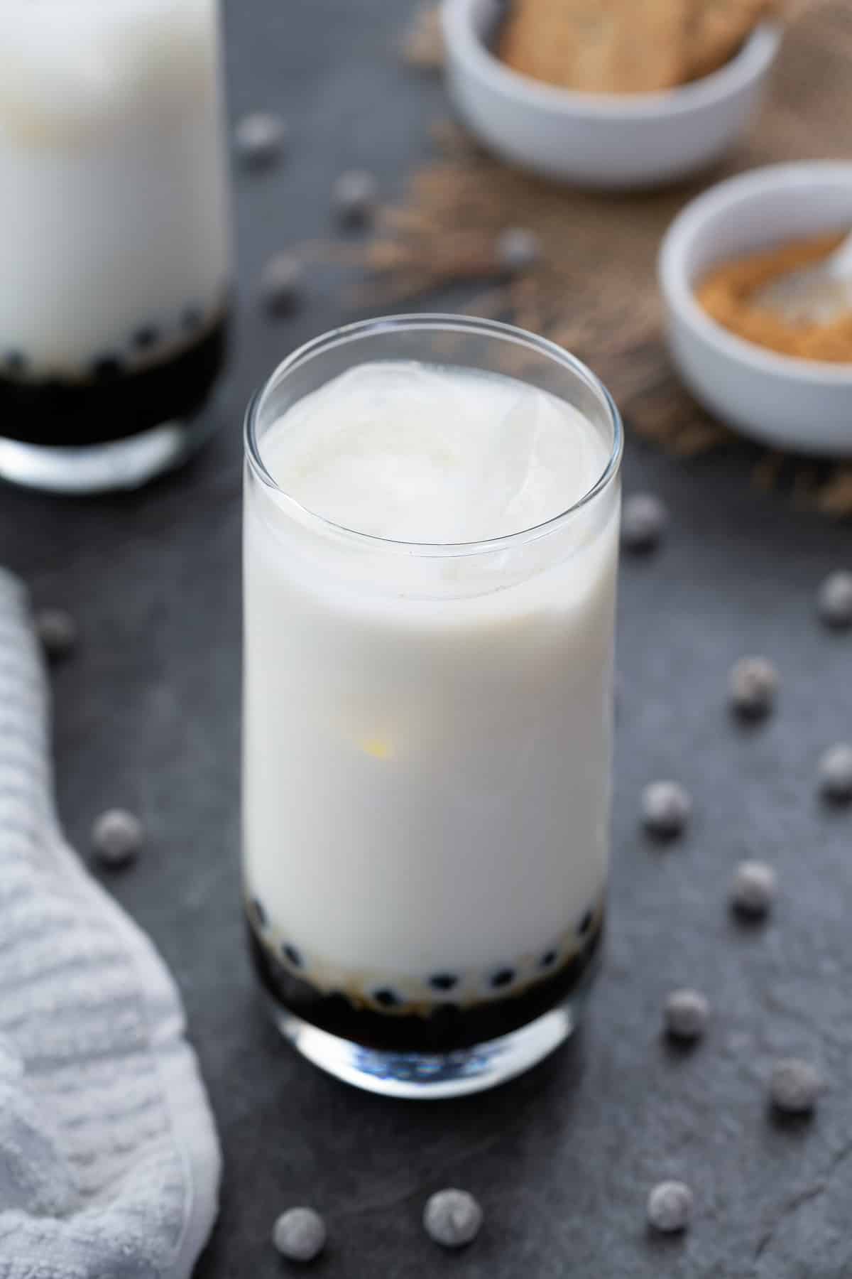 Brown Sugar boba milk served in a glass with boba pearls scattered around.