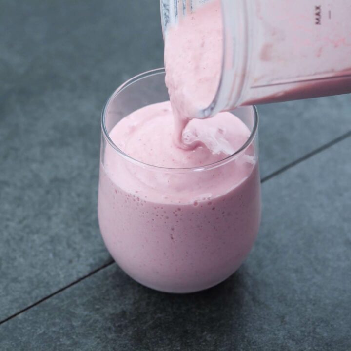Pouring strawberry smoothie into serving glass.