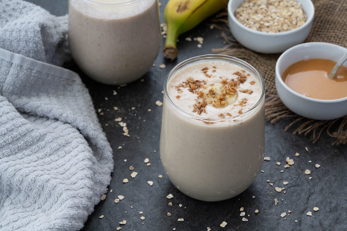 Oatmeal smoothie served in a glass with oatmeal placed in a bowl.
