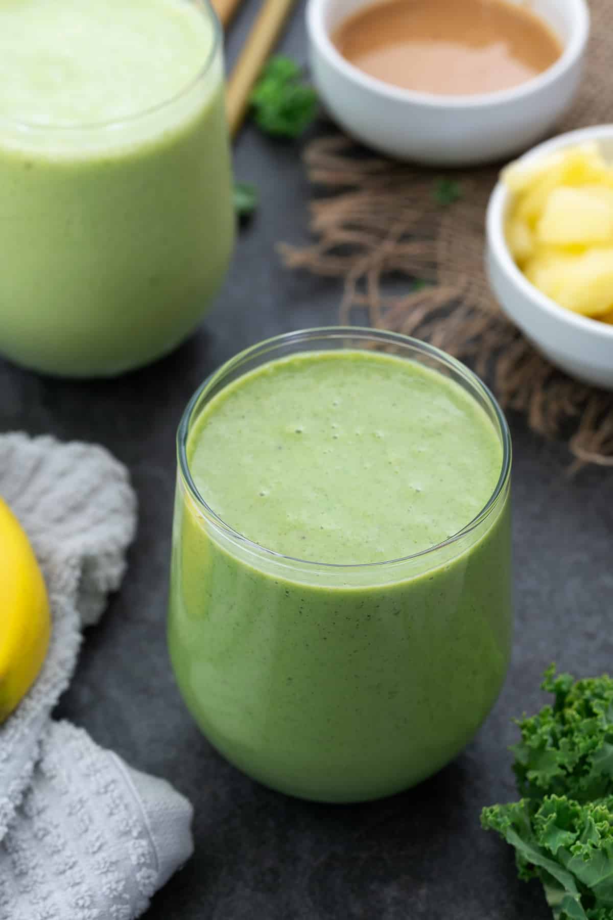 Kale Pineapple Smoothie served in a glass with pineapple and kale placed nearby.