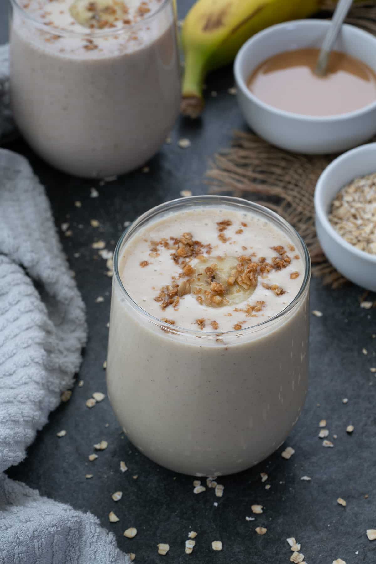 Oatmeal smoothie served in a glass with oatmeal placed in a bowl.
