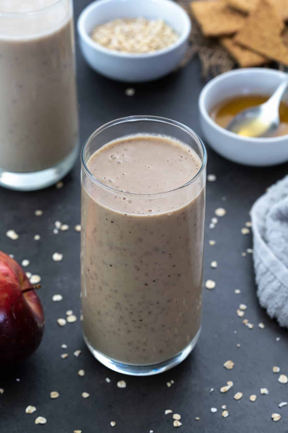 Apple Smoothie served in a glass with honey, apple and oats alongside.