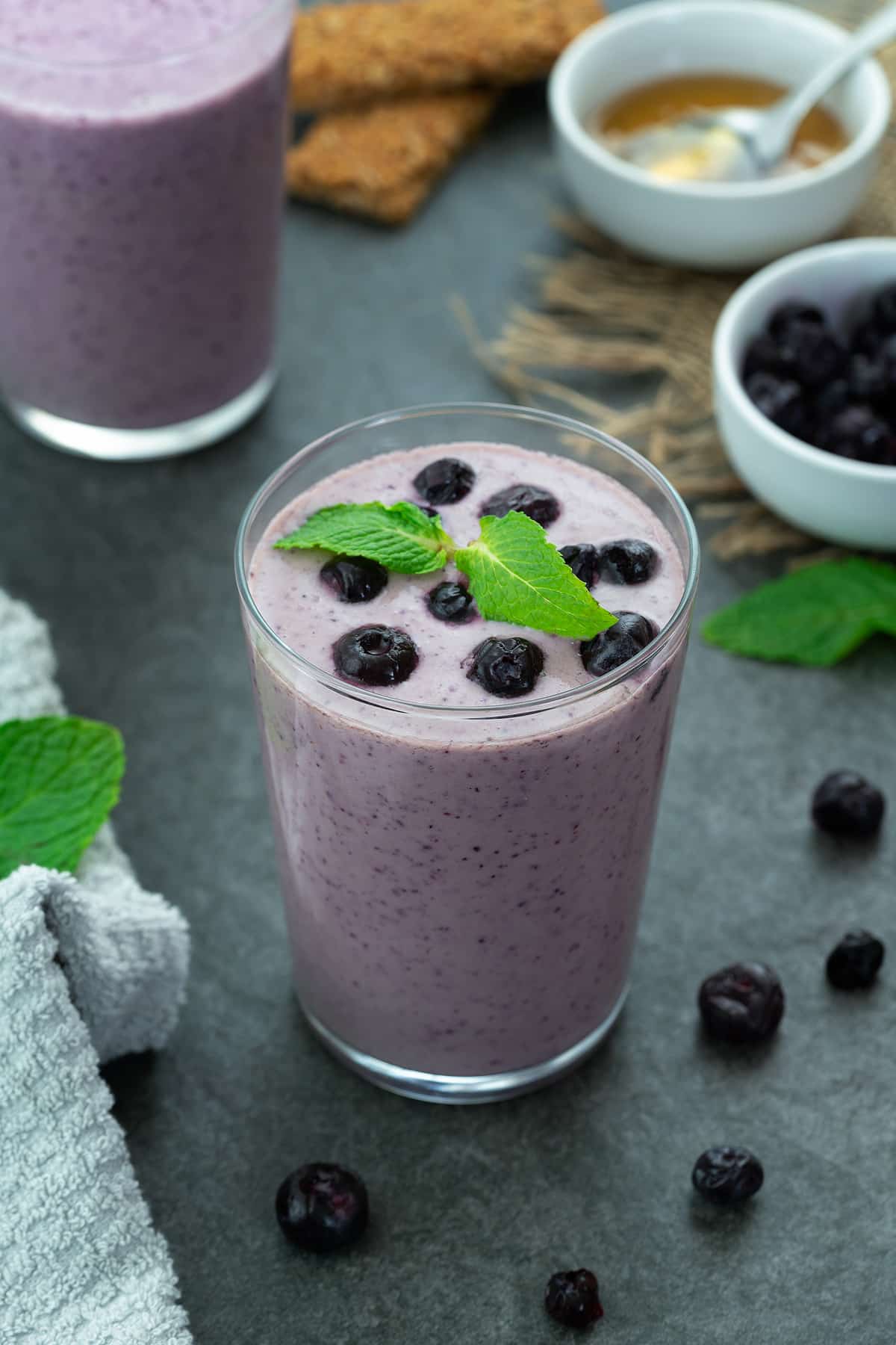 Blueberry Smoothie in a glass placed on a table with few ingredients around.