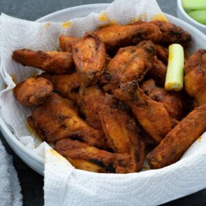 Buffalo Wings in a bowl with celery stick and sauce nearby