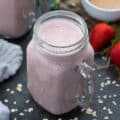 Greek yogurt smoothie served in a glass mug with strawberries and banana placed nearby.