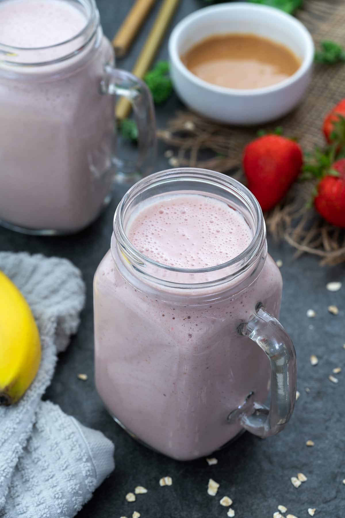 Greek yogurt smoothie served in a glass mug with strawberries and banana placed nearby.