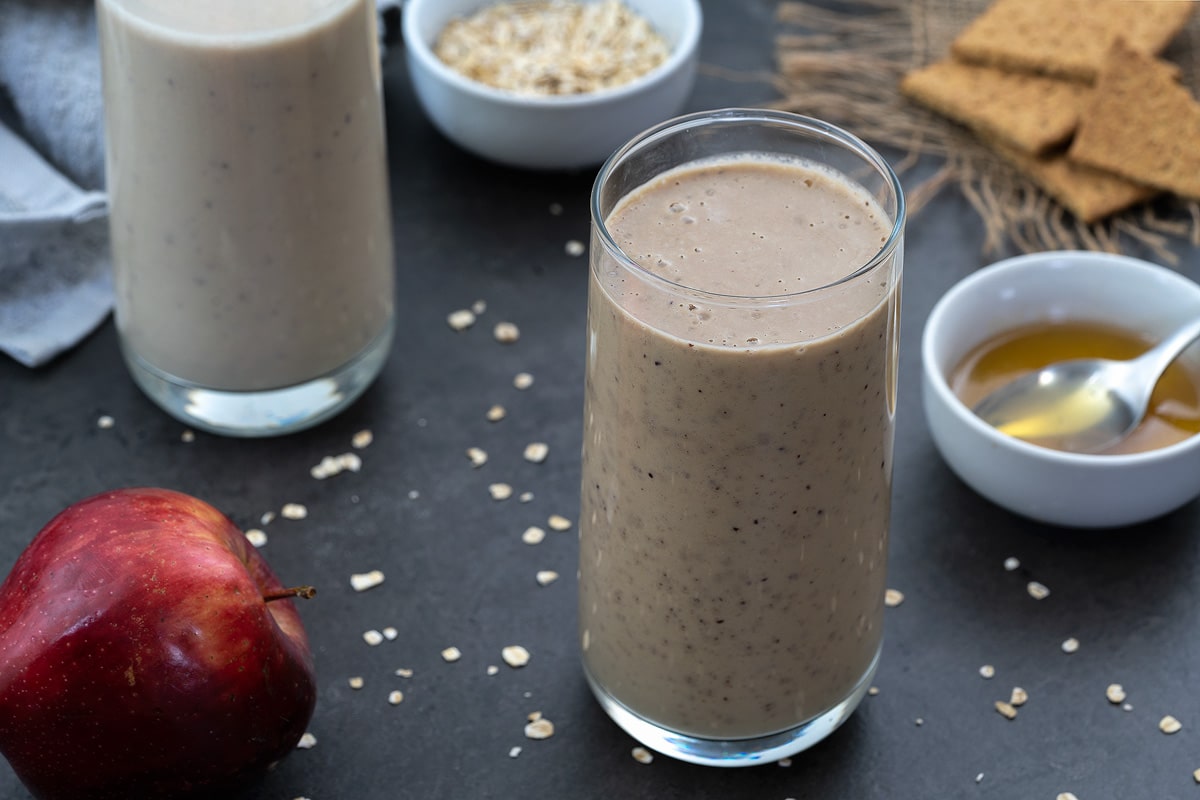 Apple Smoothie served in a glass with honey, apple and oats alongside.