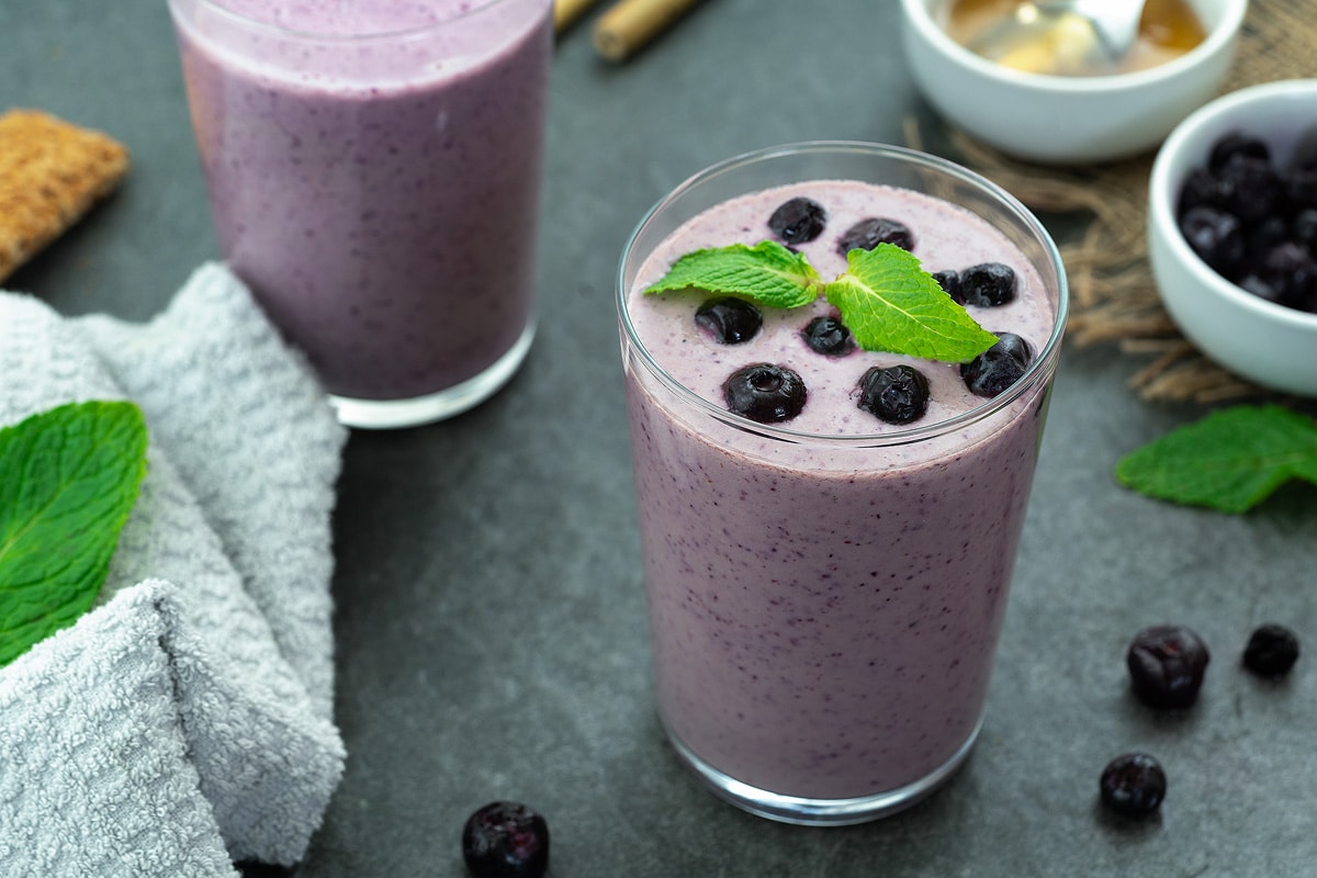 Blueberry Smoothie in a glass placed on a table with few ingredients around.