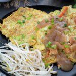 Egg Foo Young served in a black plate with lemon and cabbage in a cup nearby