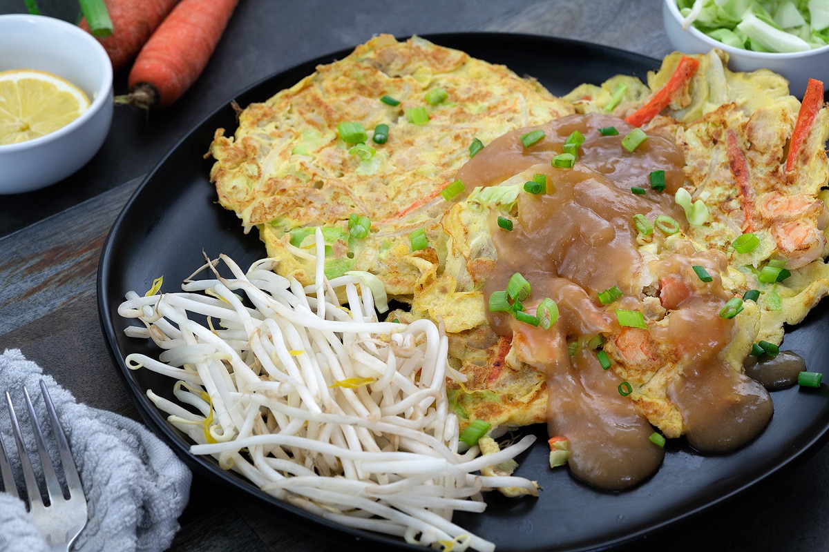 Egg Foo Young served in a black plate with lemon and cabbage in a cup nearby