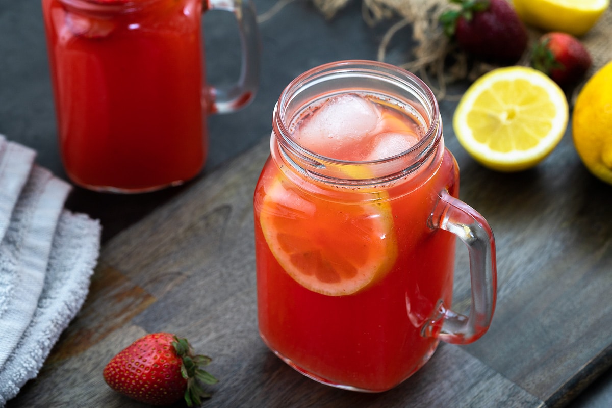 Strawberry Lemonade in a glass mug placed on a table with lemon and strawberry nearby.