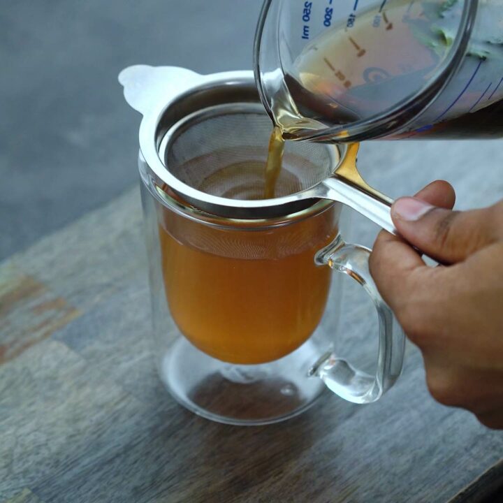 Filtering a green mint tea into a serving cup.