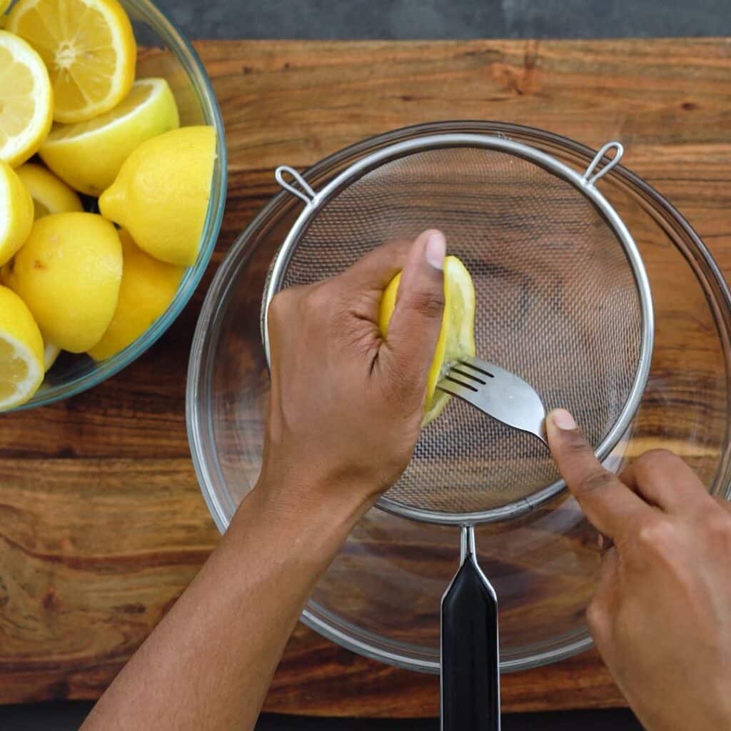 Squeezing the lemon juice over a mesh strainer.