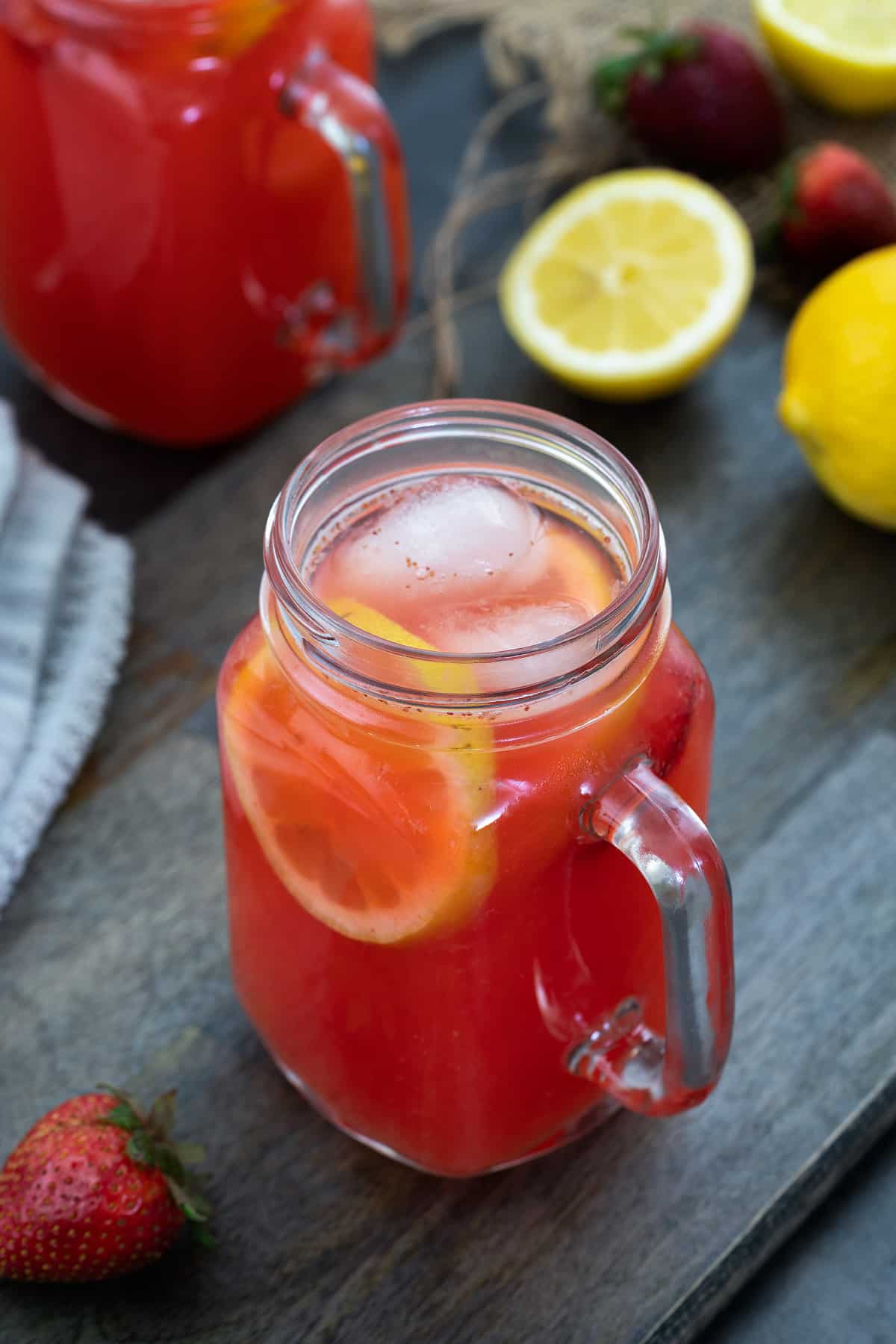 Strawberry Lemonade in a glass mug placed on a table with lemon and strawberry nearby.