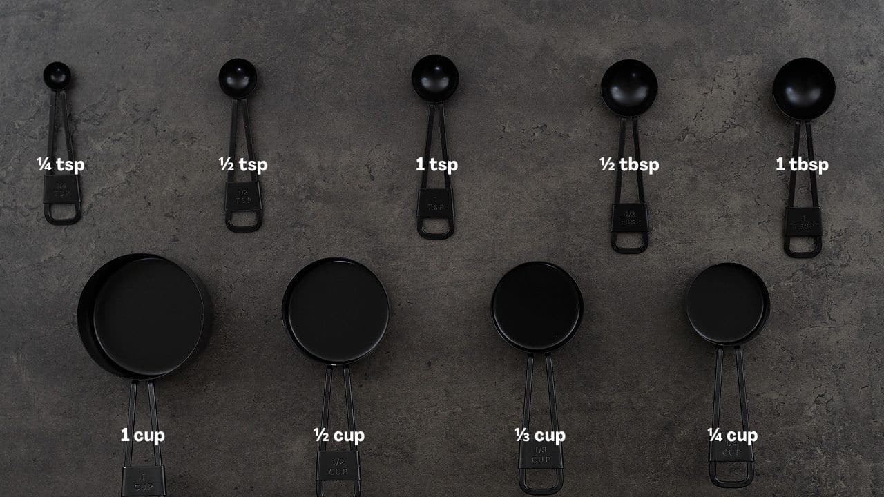 Black color US Kitchen Measurement Cups and Spoons placed on a grey table