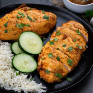 Air fryer chicken breast served in a black plate with rice and cucumber