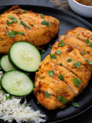 Air fryer chicken breast served in a black plate with rice and cucumber