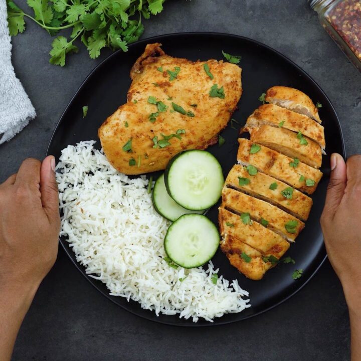Serving air fryer chicken breast with rice and cucumber on a black plate