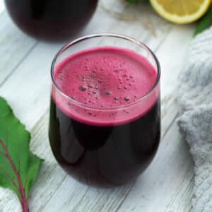 Beetroot juice in glass placed on a whiteboard with lemon and beet leaf alongside.