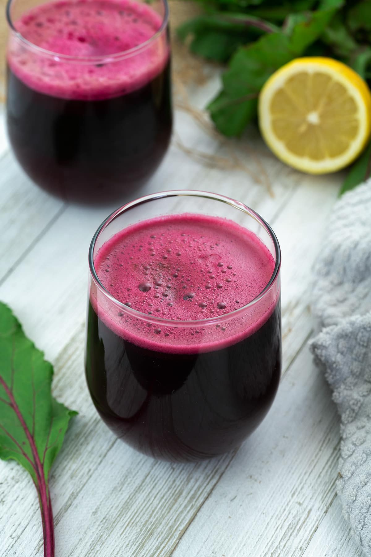 Beetroot juice in glass placed on a whiteboard with lemon and beet leaf alongside.