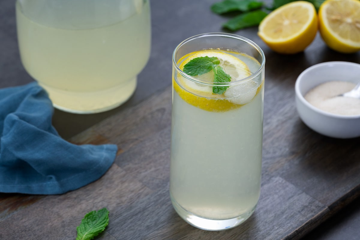 Fresh Lemon Juice in a glass placed on a grey table with sugar and cut lemon alongside.