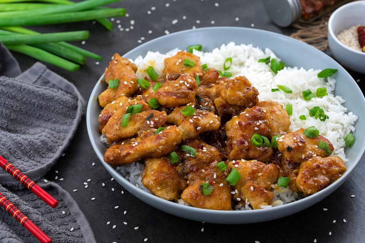 Orange chicken in a white place with rice and placed on a gray table