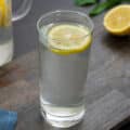 Lemon water in a glass with cut lemon on a grey table.