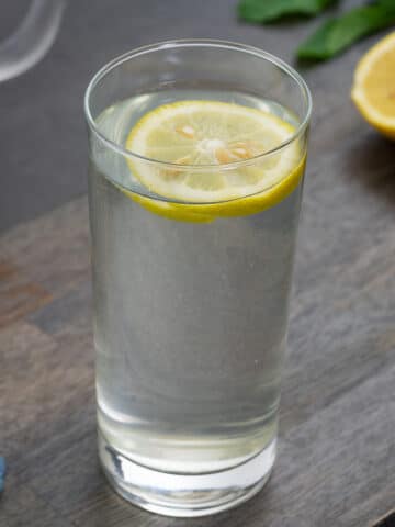 Lemon water in a glass with cut lemon on a grey table.