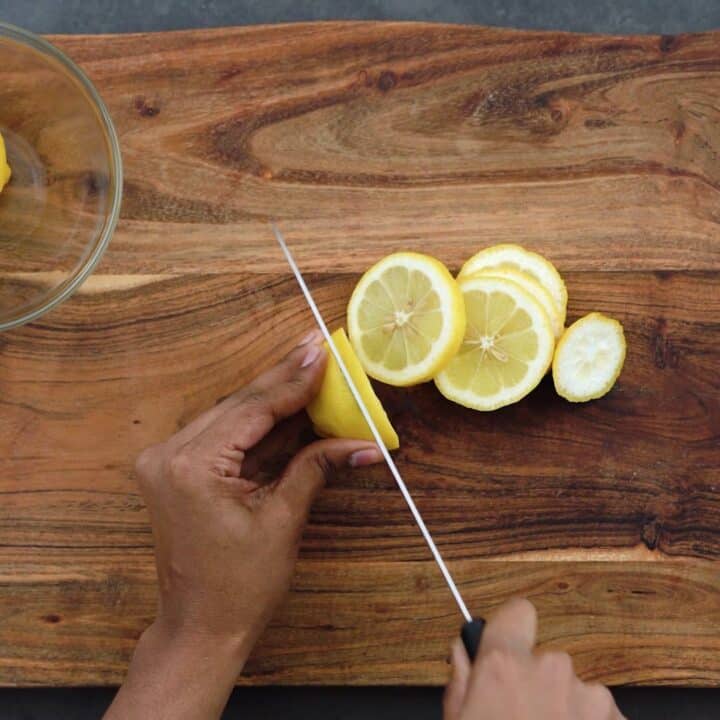 Slicing the lemons with knife on a cutting board.