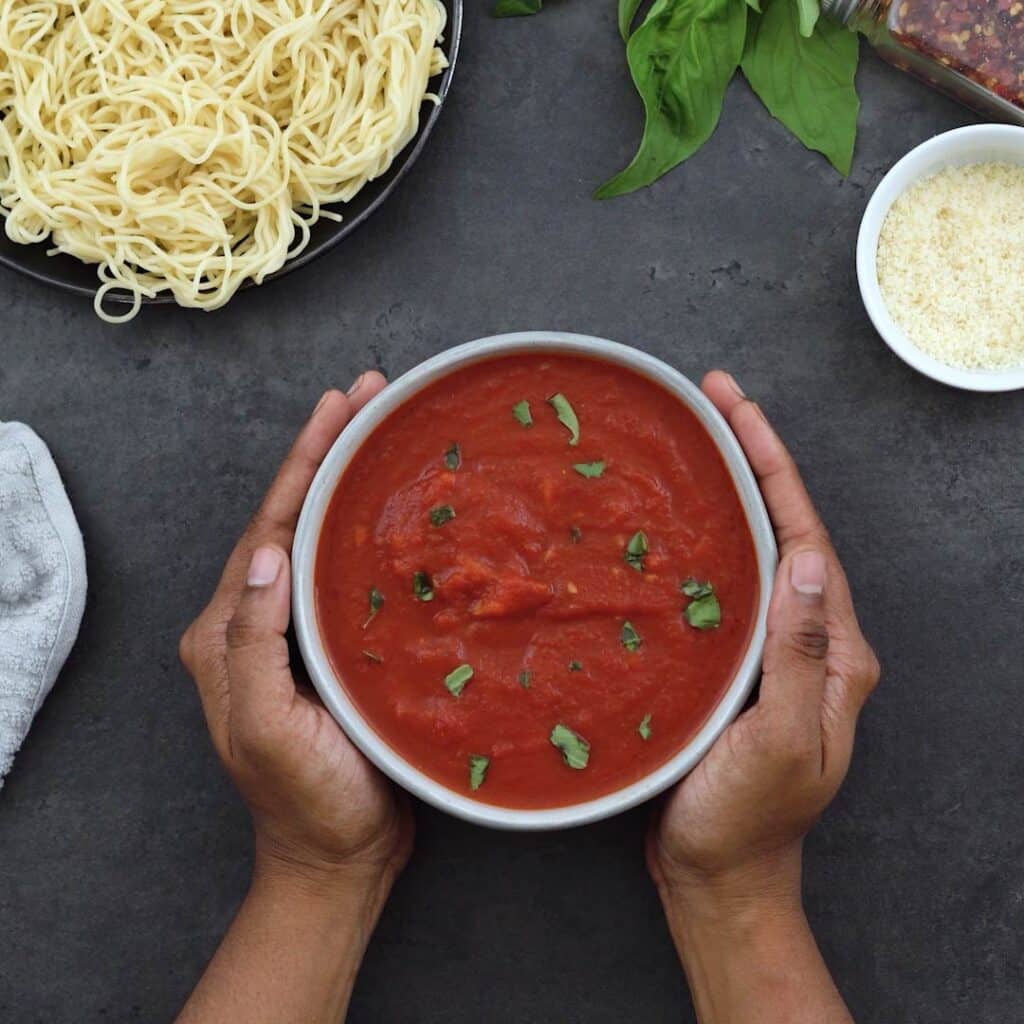 Serving Marinara Sauce in a white bowl with pasta and cheese alongside