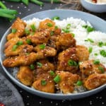 Orange chicken in a white plate with rice and placed on a grey table