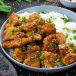Orange chicken in a white bowl with rice and placed on a grey table