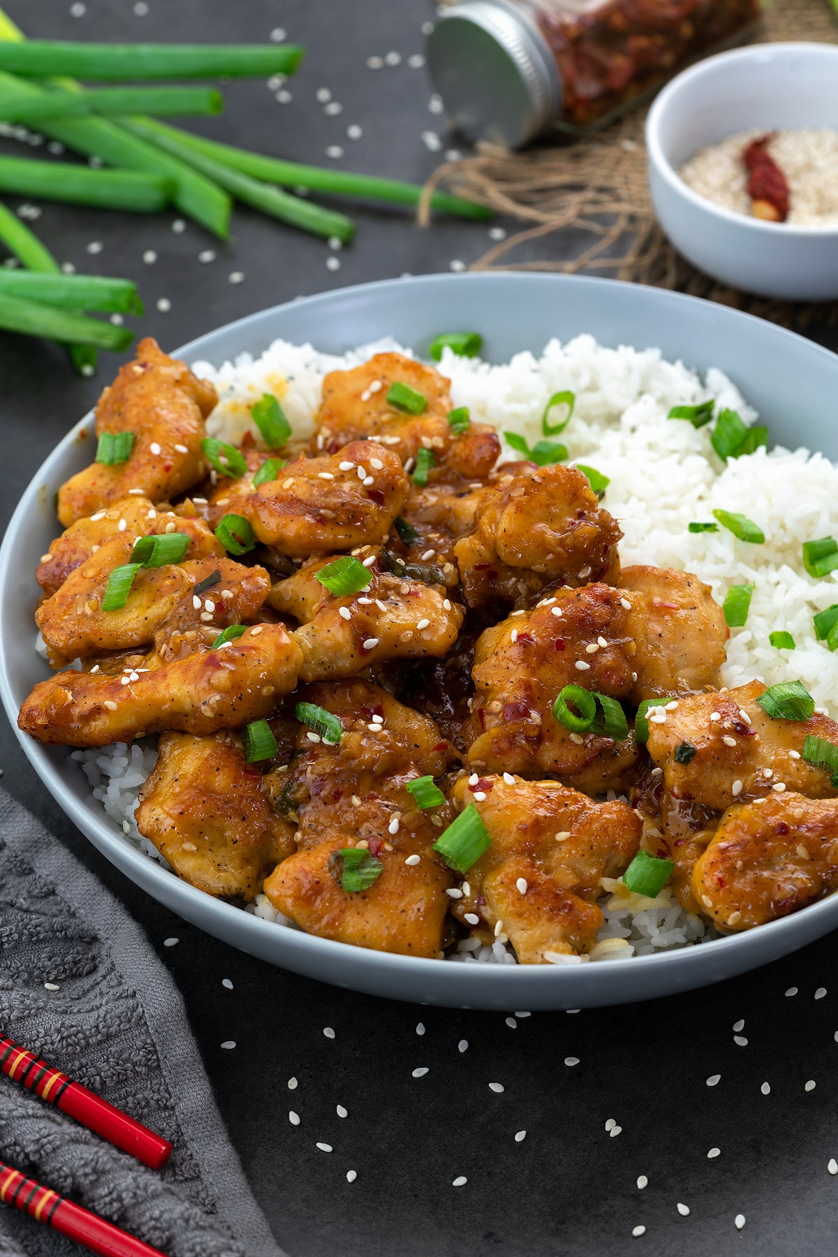 Orange chicken in a white bowl with rice and placed on a grey table