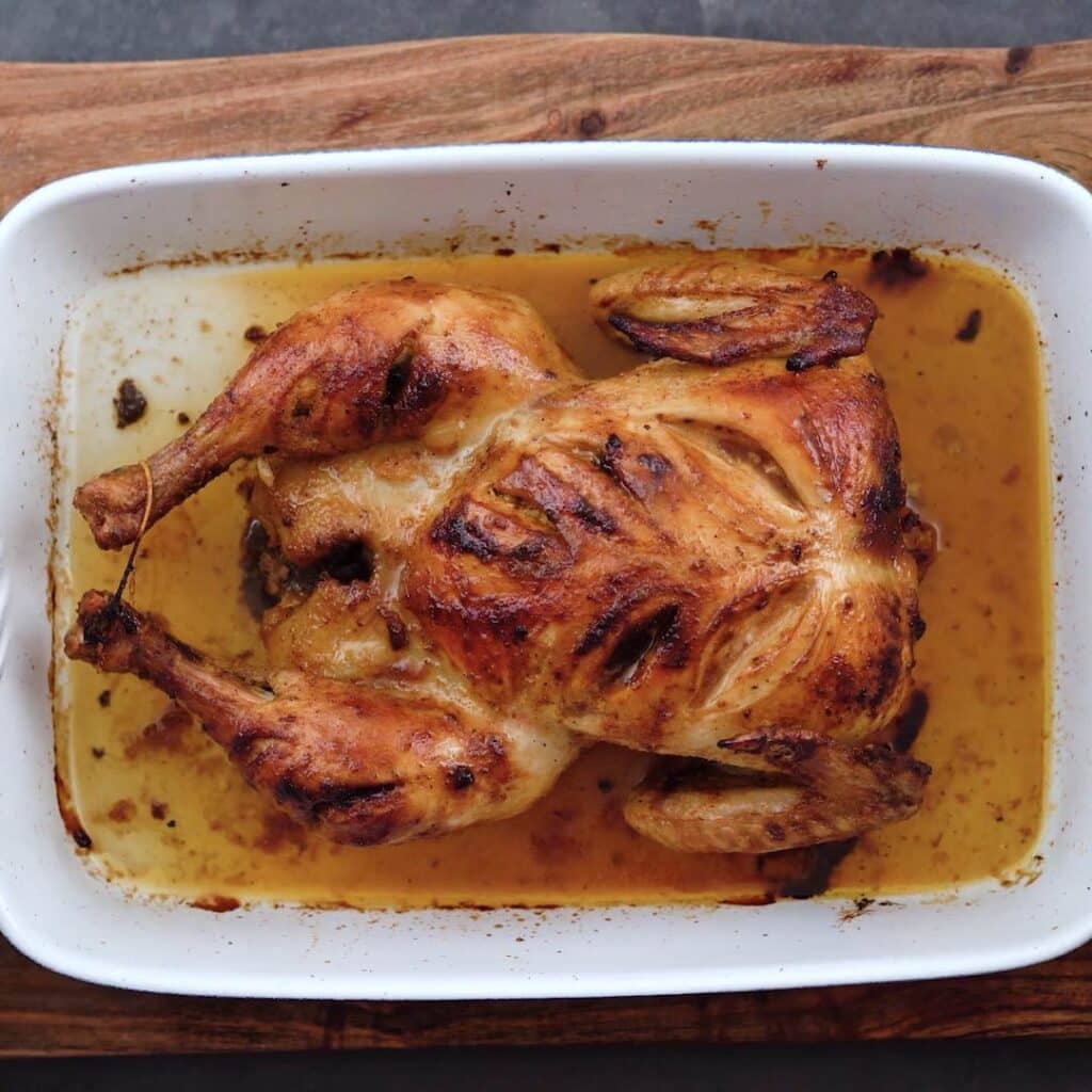 Roasted chicken in a white ceramic tray with pan juices