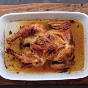 Roasted chicken in a white ceramic tray with pan juices