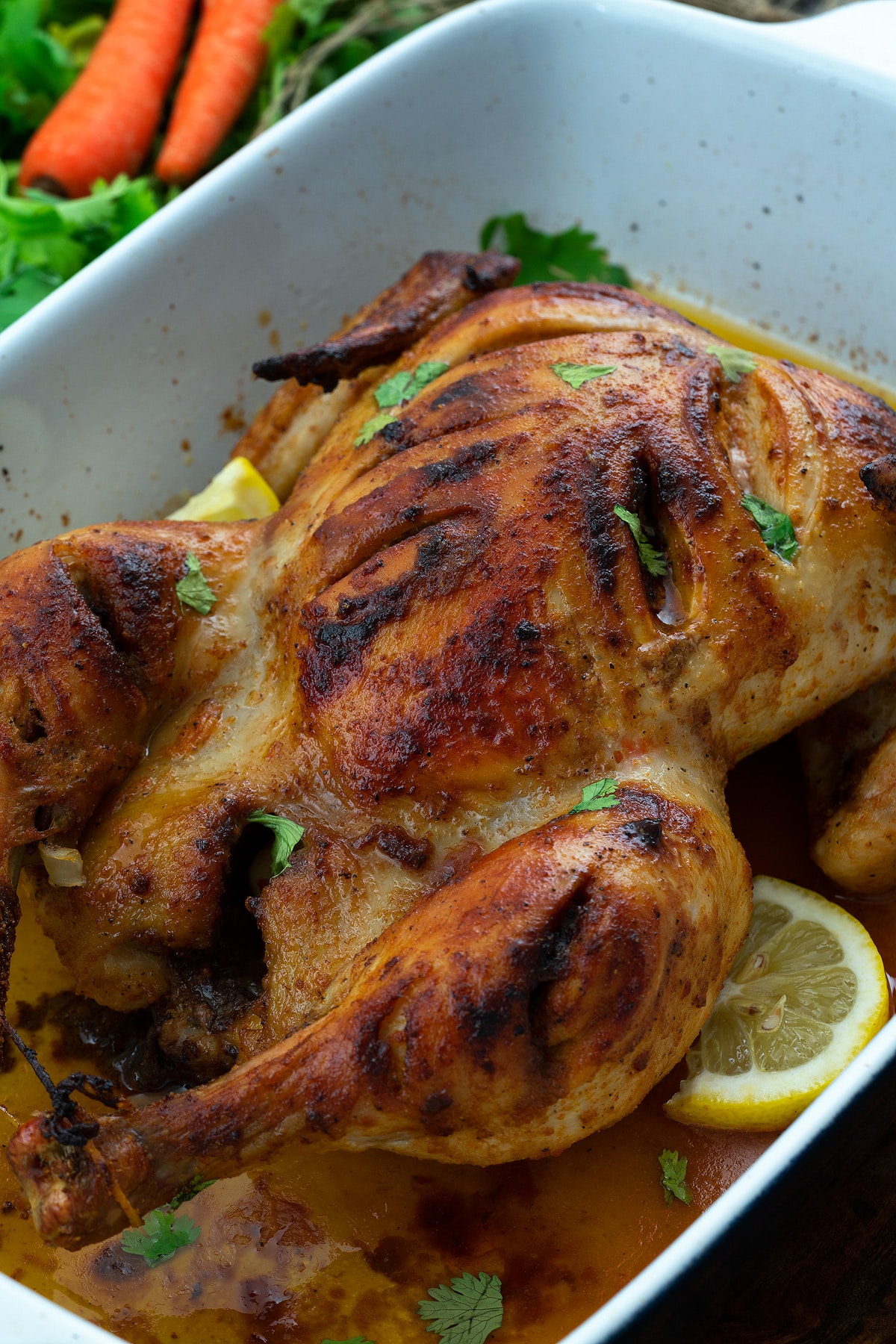 Whole roasted chicken in a white ceramic baking tray with lemon slices