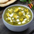 Palak Paneer served in a white bowl and placed on a grey table with naan nearby
