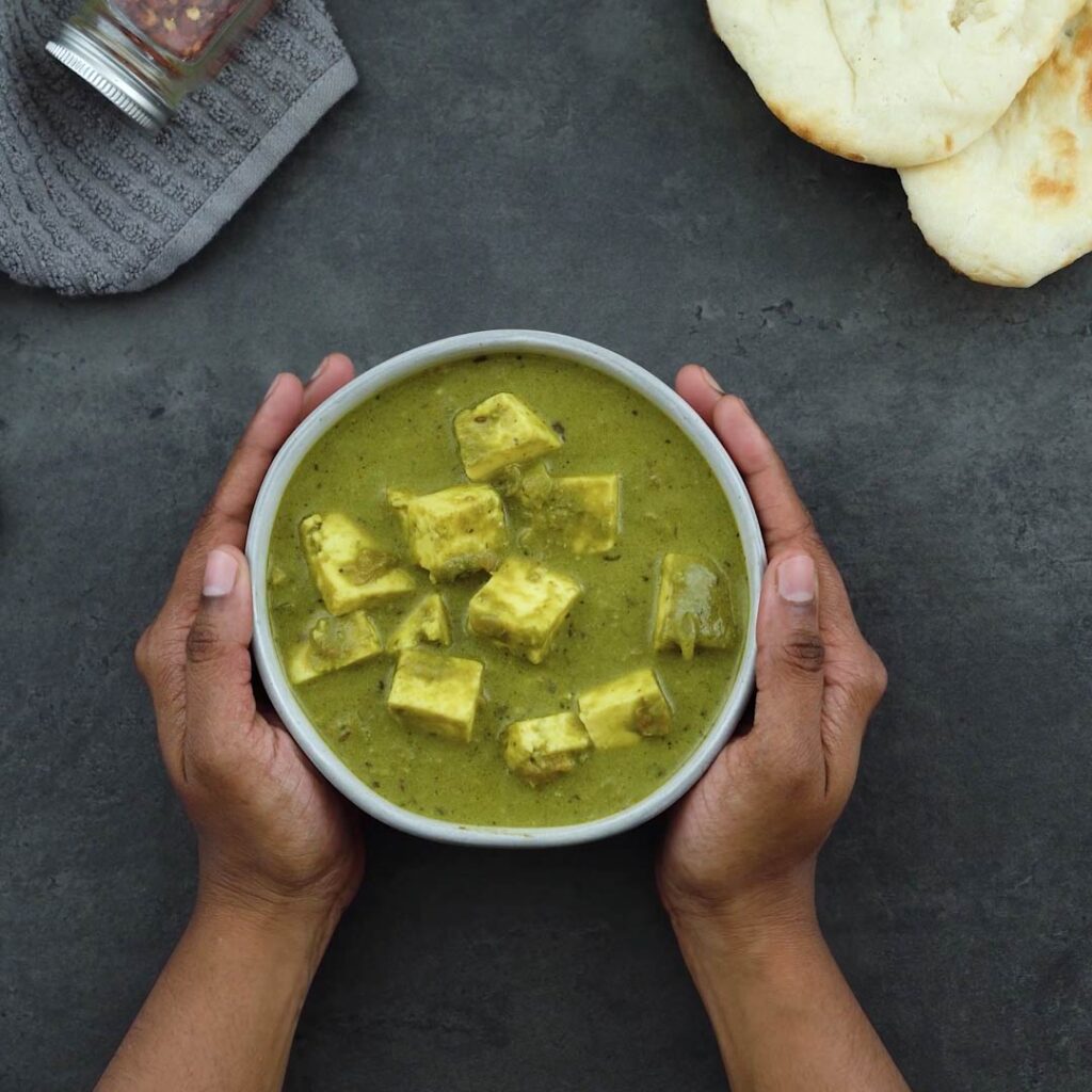 Palak Paneer is served in a white bowl with naan alongside