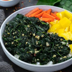 Sauteed spinach in a white bowl with carrot and yellow bell pepper pieces