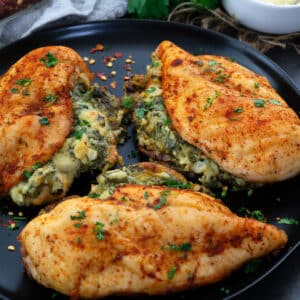 Spinach stuffed chicken breasts in a black plate with cheese alongside in a cup