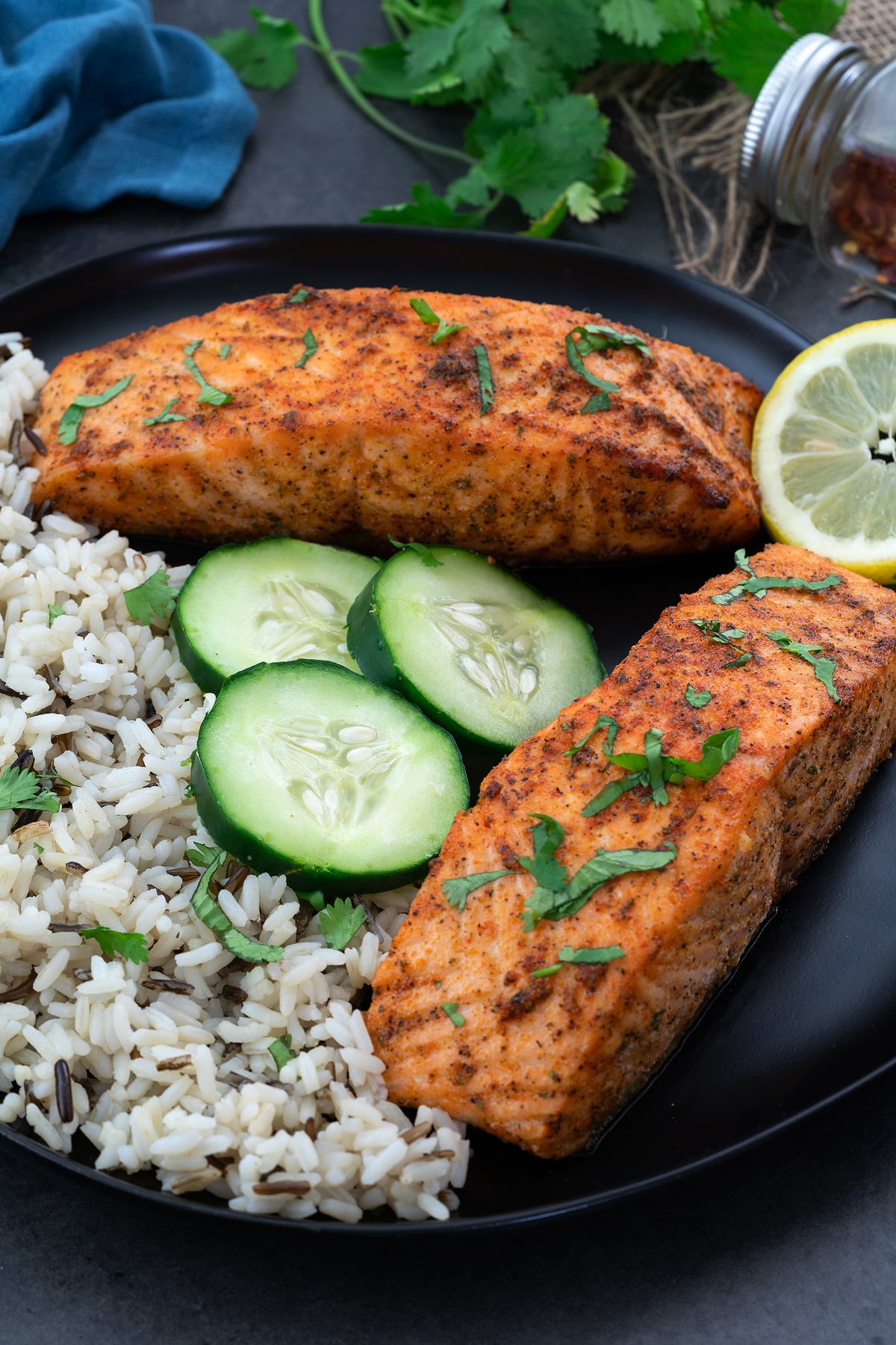 Air Fried Salmon Fillets in a black plate with rice, cucumber and lemon slices.