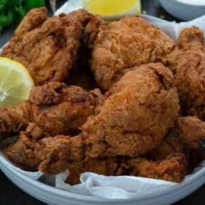 Fried chicken legs and thighs in a white bowl with lemon slice and sauces around