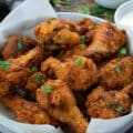 Fried Chicken wings in a white bowl along with sauces in cups.