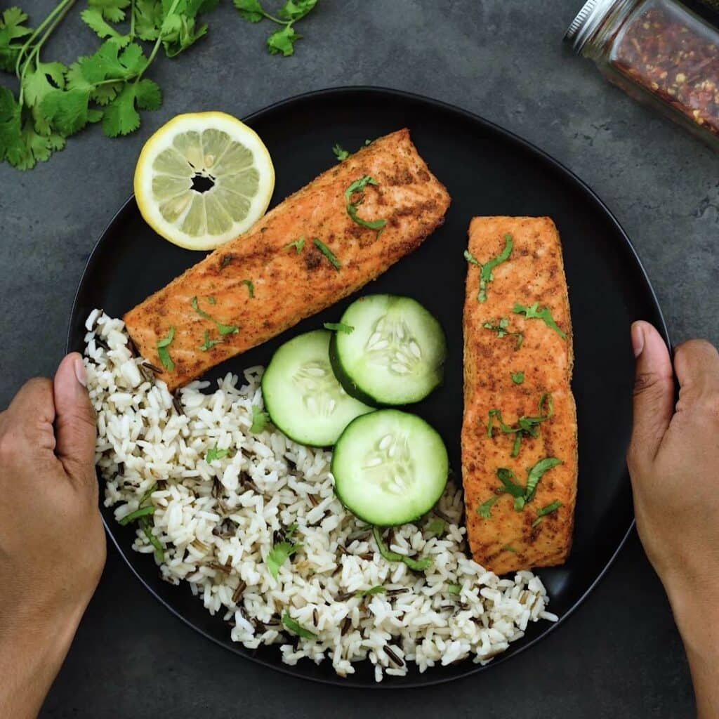 Serving healthy Air Fryer Salmon with white and wild rice in a black plate.