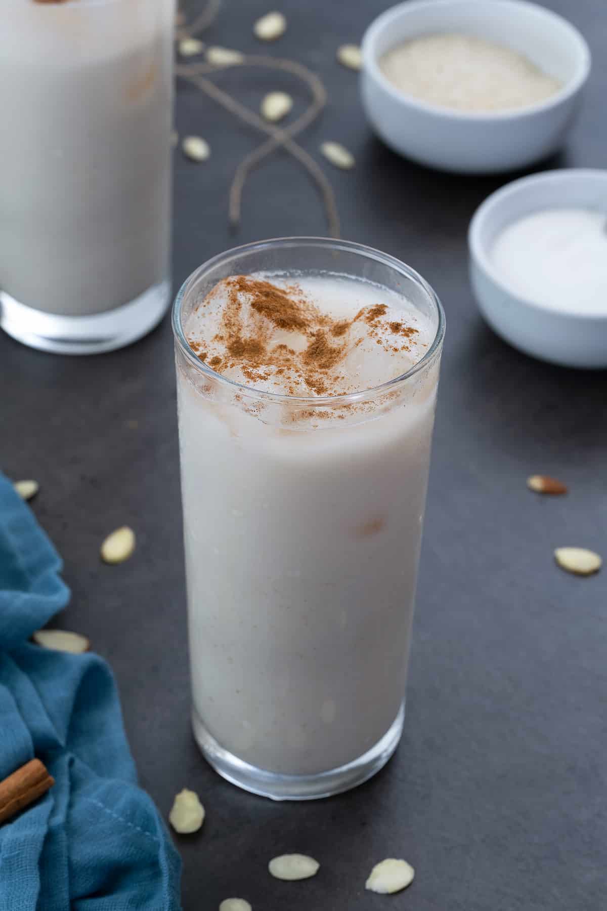 Horchata is in two glasses with few ingredients in cups and a blue towel around.