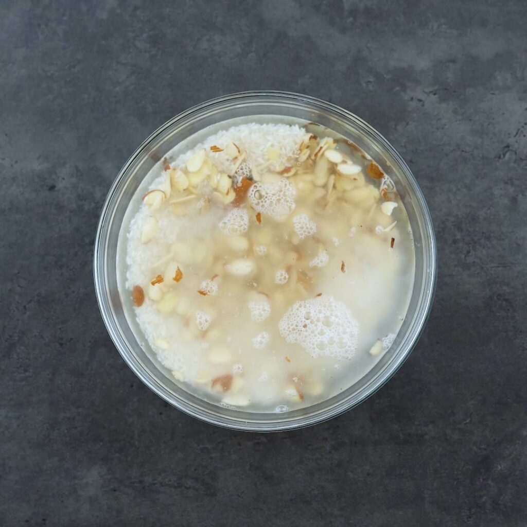 Rice, almonds and cinnamon stick soaking in water in a a glass bowl.