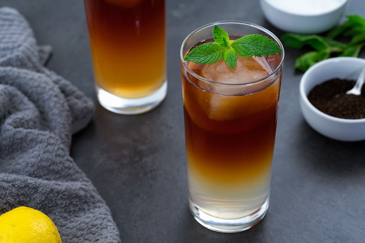 Arnold Palmer drink in a glass placed on a grey table with few ingredients around.