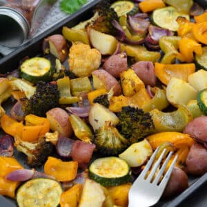 Roasted vegetables in a baking tray with rice in a plate alongside