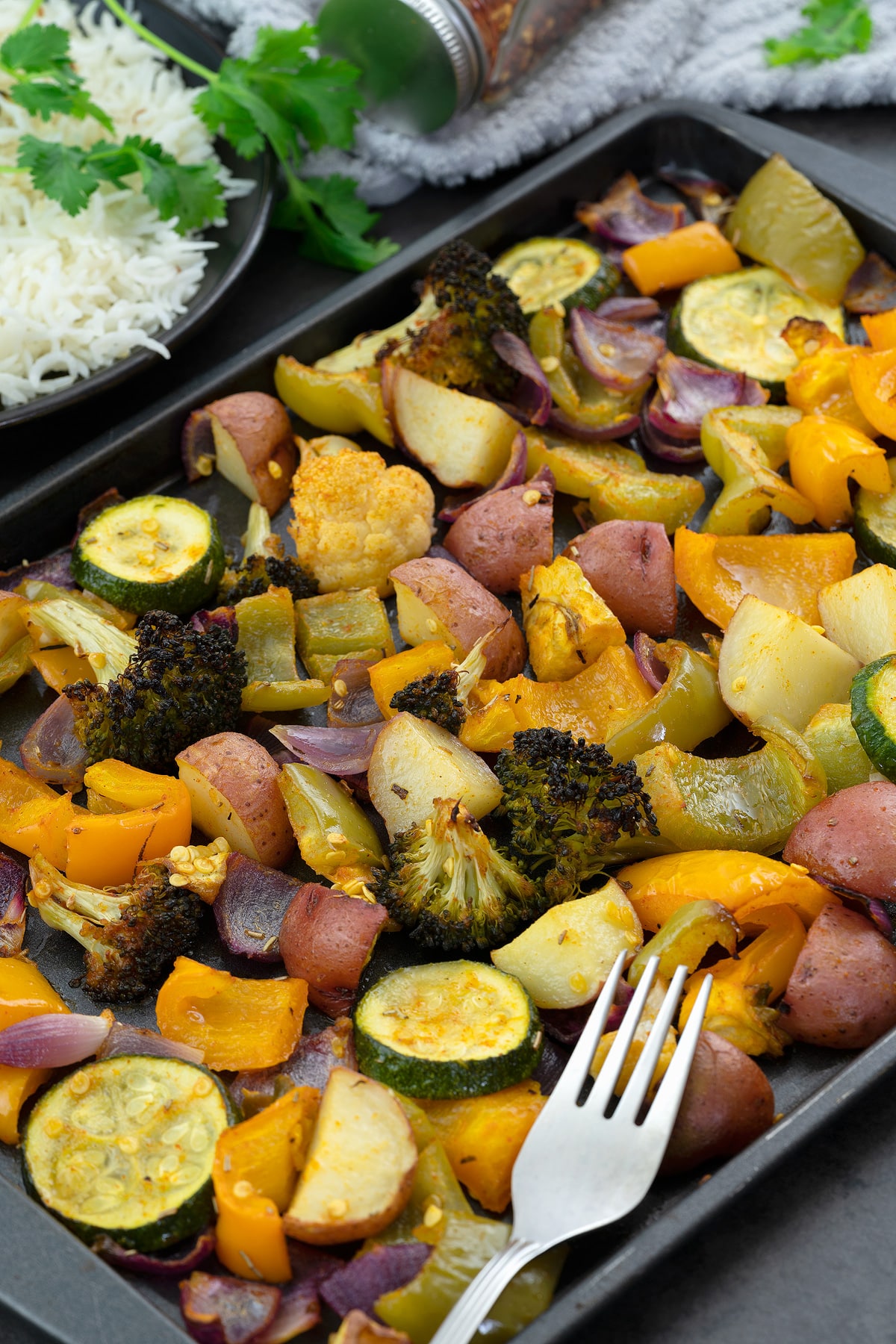 Oven roasted vegetables in a baking tray with rice in a plate alongside